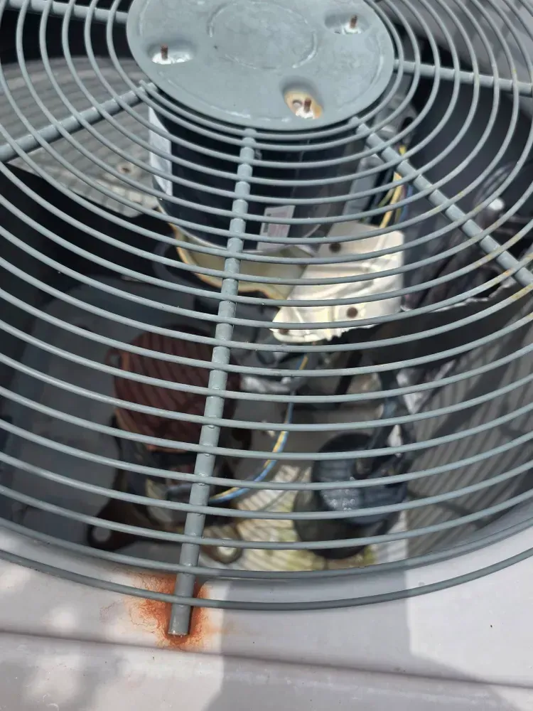 Close-up of an air conditioning unit fan with a protective metal grill.