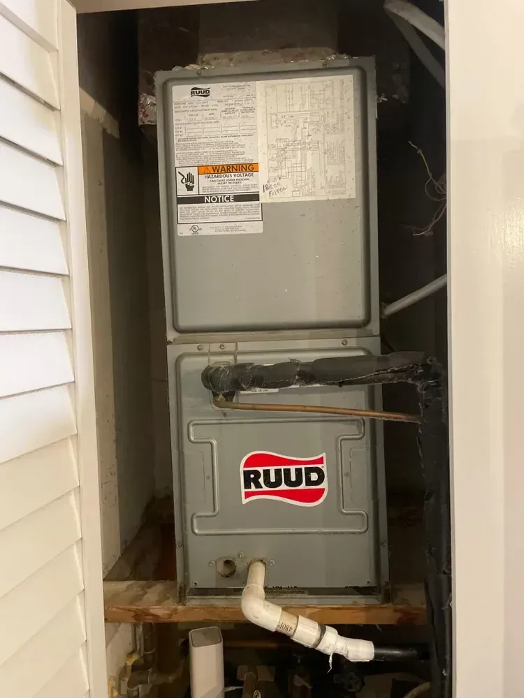 Rudd furnace in a closet, white and gray. The unit is open. A white pipe is connected.