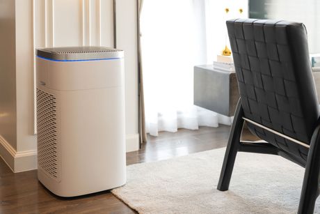 White air purifier in a modern living room setting, near a window and a black chair.
