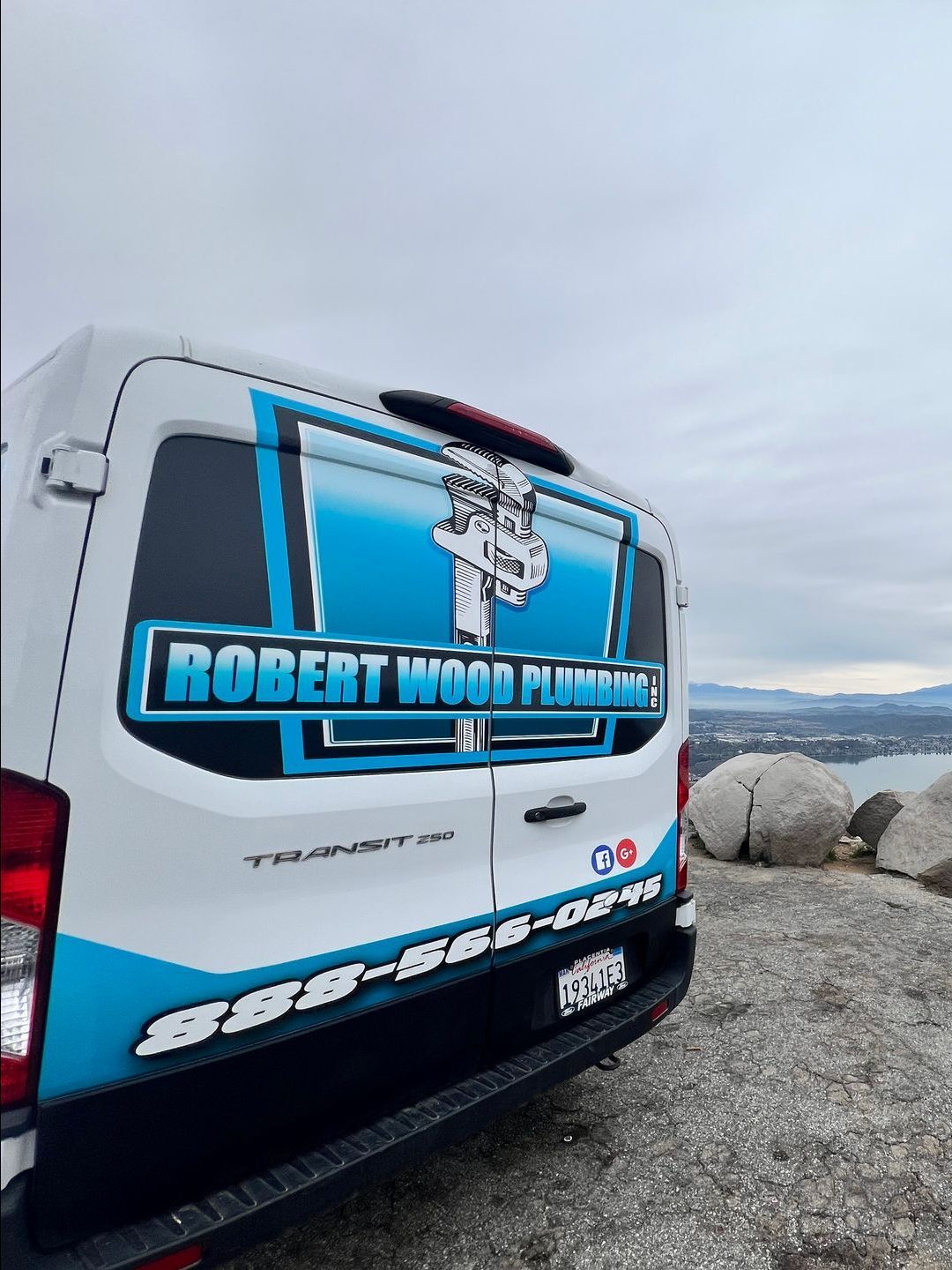 A robert wood plumbing van is parked on a rocky beach.