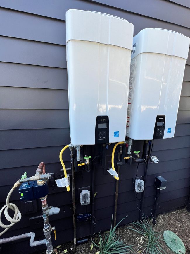 Two white water heaters are attached to the side of a house