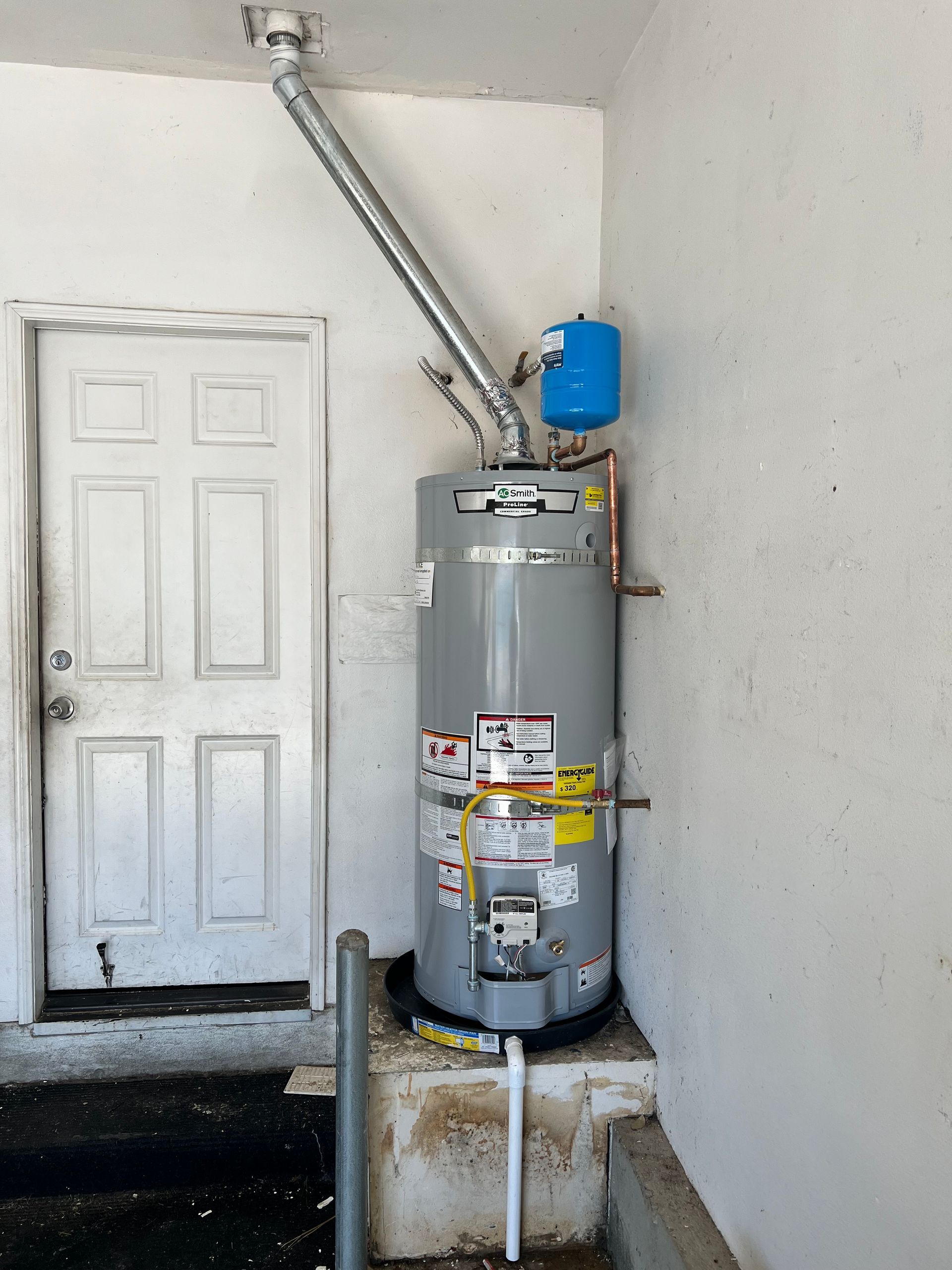 A water heater is sitting next to a door in a garage.