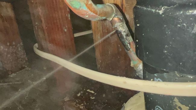 A copper pipe is leaking water in a basement.