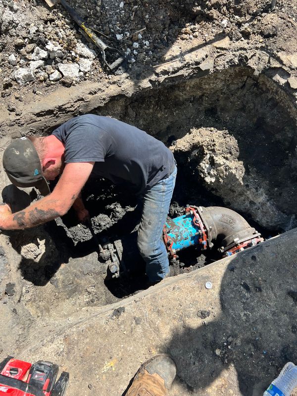 A man is working on a pipe in the dirt.