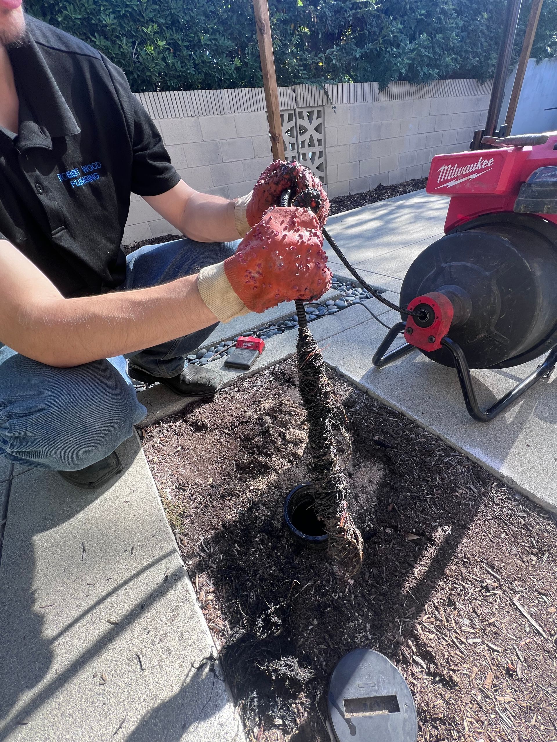 A man is kneeling down next to a machine that is cleaning a drain.