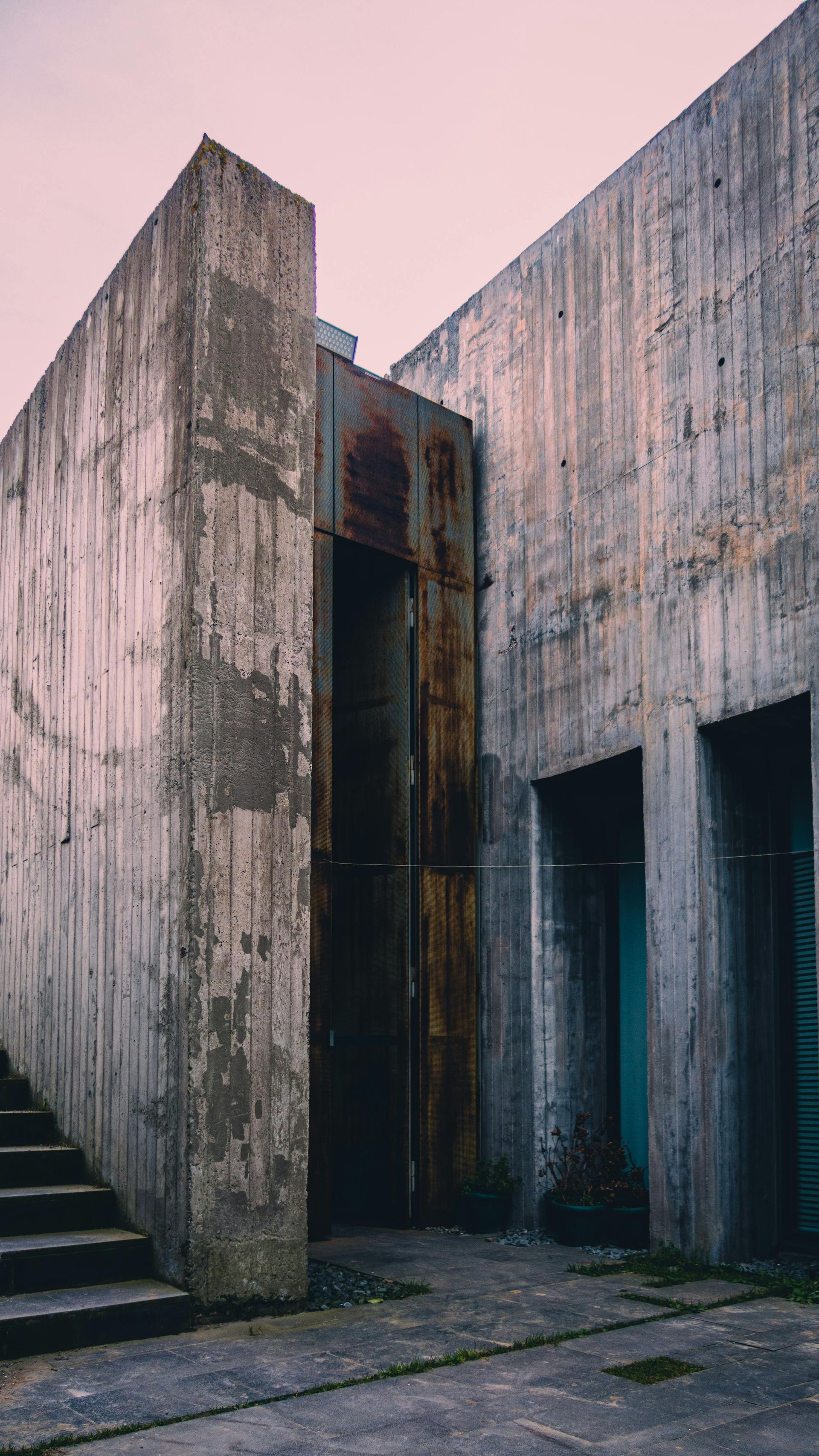 A concrete building with stairs leading up to it and a rusty door.