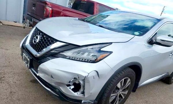 Silver Nissan Murano SUV with front-end damage; headlight missing, dented hood and bumper.