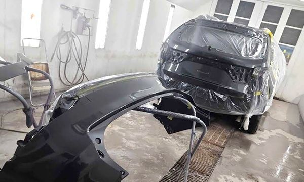 Car parts, covered in plastic, in a spray painting booth.