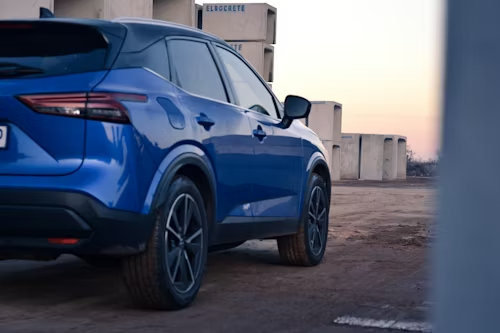A blue SUV parked outdoors at sunset, viewed from the rear three-quarter angle against a background of concrete blocks.