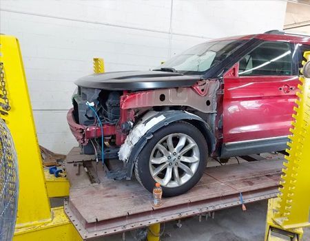 Red car undergoing repair in a shop; front end disassembled on a lift.