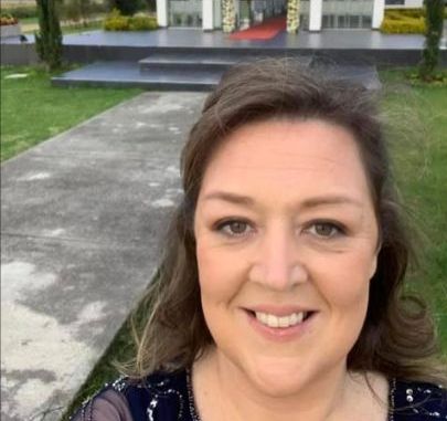 Smiling woman taking a selfie outdoors with a white structure with a red carpet in the background.