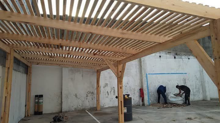 Dos trabajadores instalando una losa de hormigón bajo una pérgola de madera en el exterior.