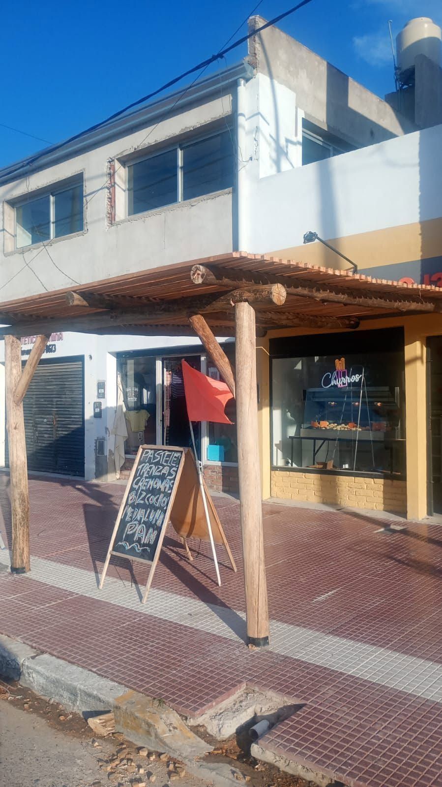 Cafetería a pie de calle con toldo de madera, cartel de pizarra y escaparate bajo un cielo azul.