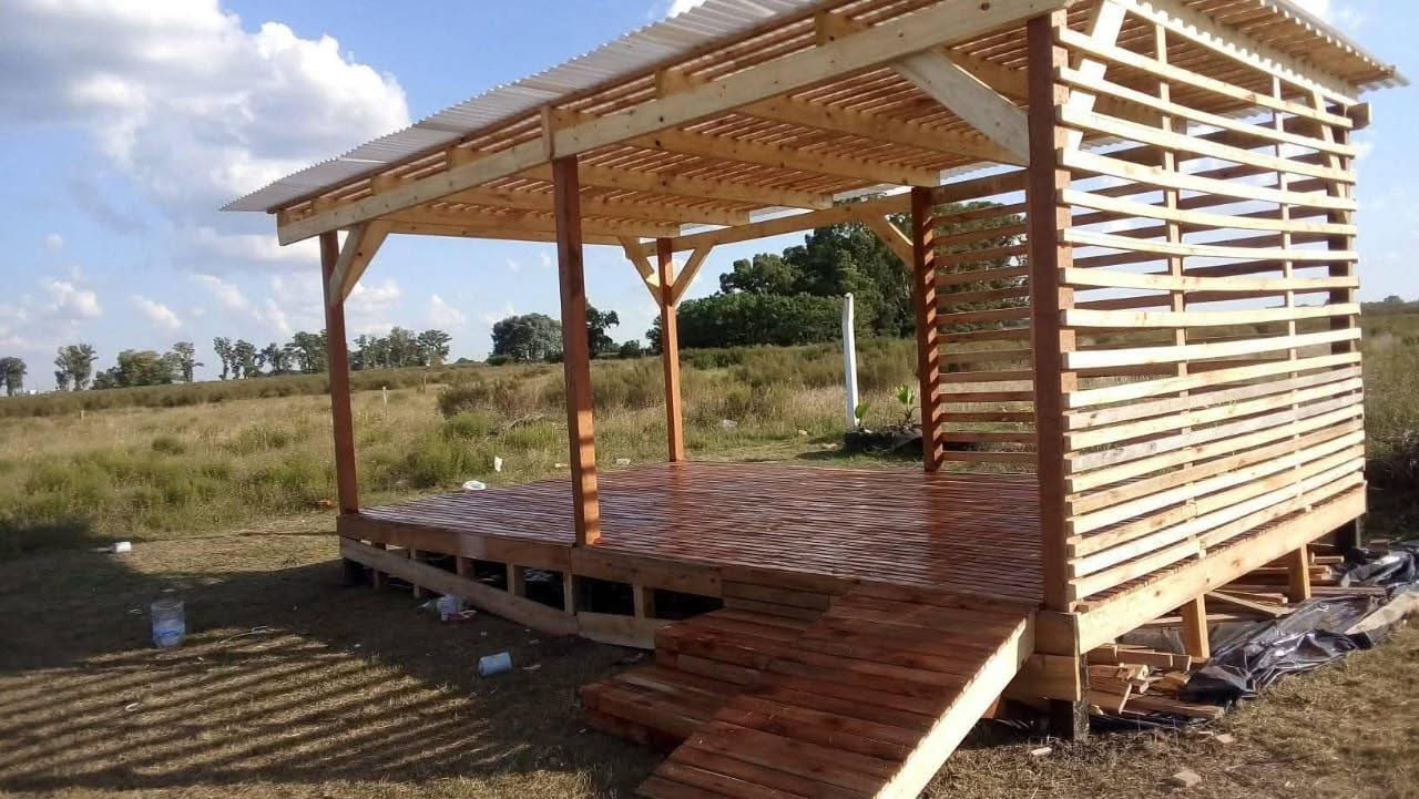 Pequeña cabaña de madera sin terminar con paredes de listones y porche en un campo de hierba 