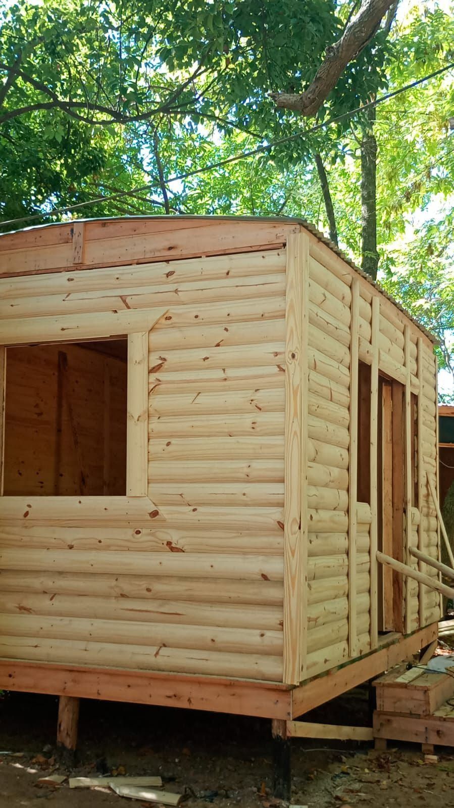Cabaña de madera parcialmente construida sobre una base elevada entre árboles.