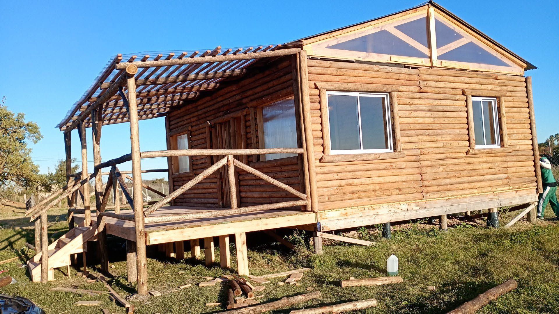 Cabaña de madera sobre pilotes con porche y techo inclinado en un entorno exterior cubierto de césped.