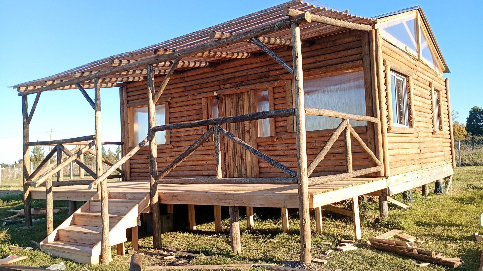 Casa de madera en construcción con porche elevado, escaleras y estructura de techo sin terminar 