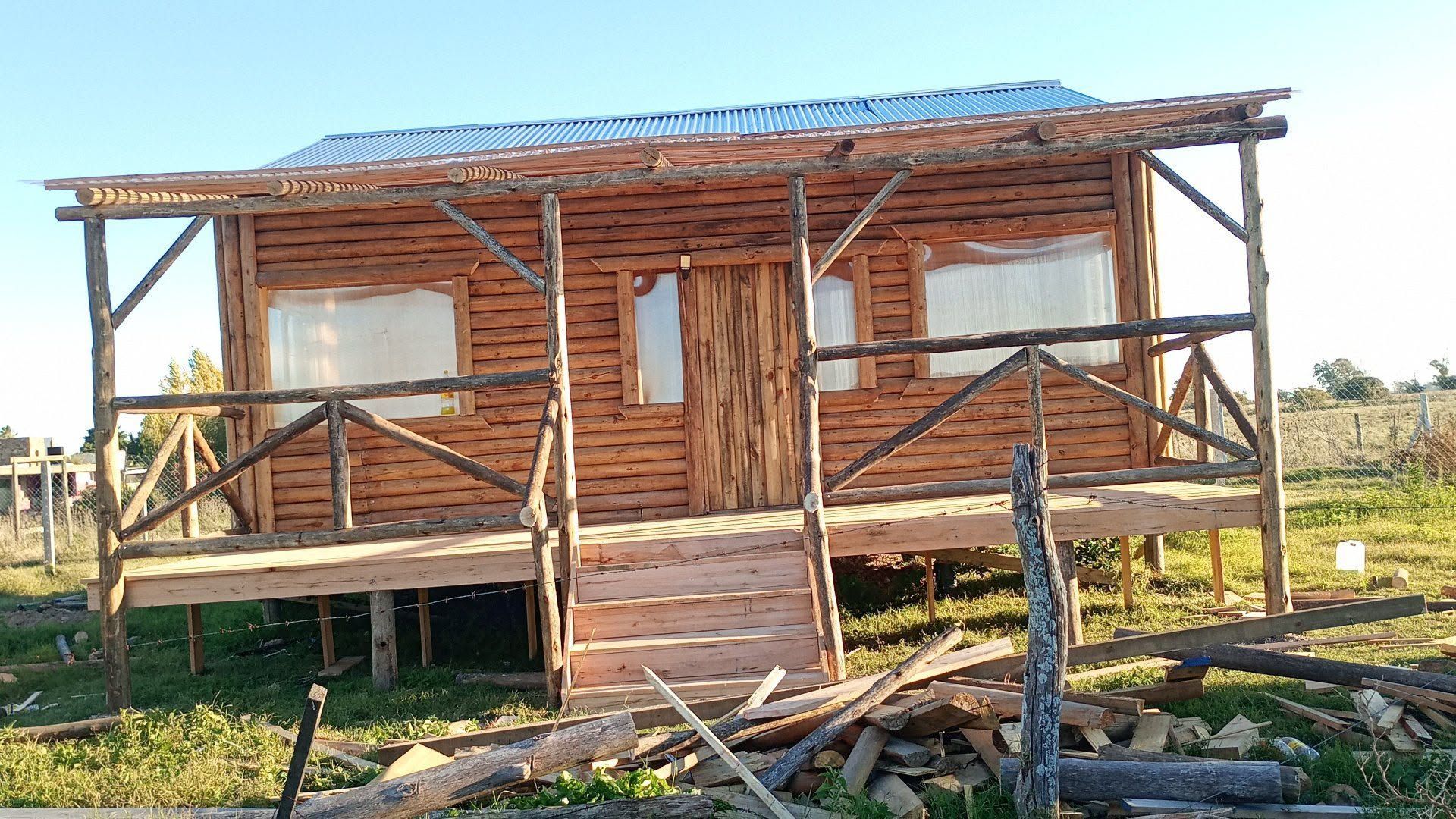 Pequeña casa rústica de madera con porche delantero y escalones en un campo soleado.