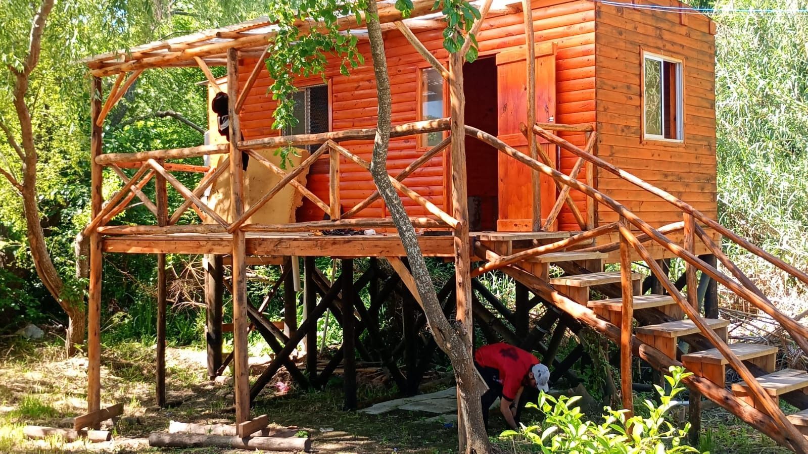 Casa de madera sobre pilotes en construcción con revestimiento naranja, escaleras 