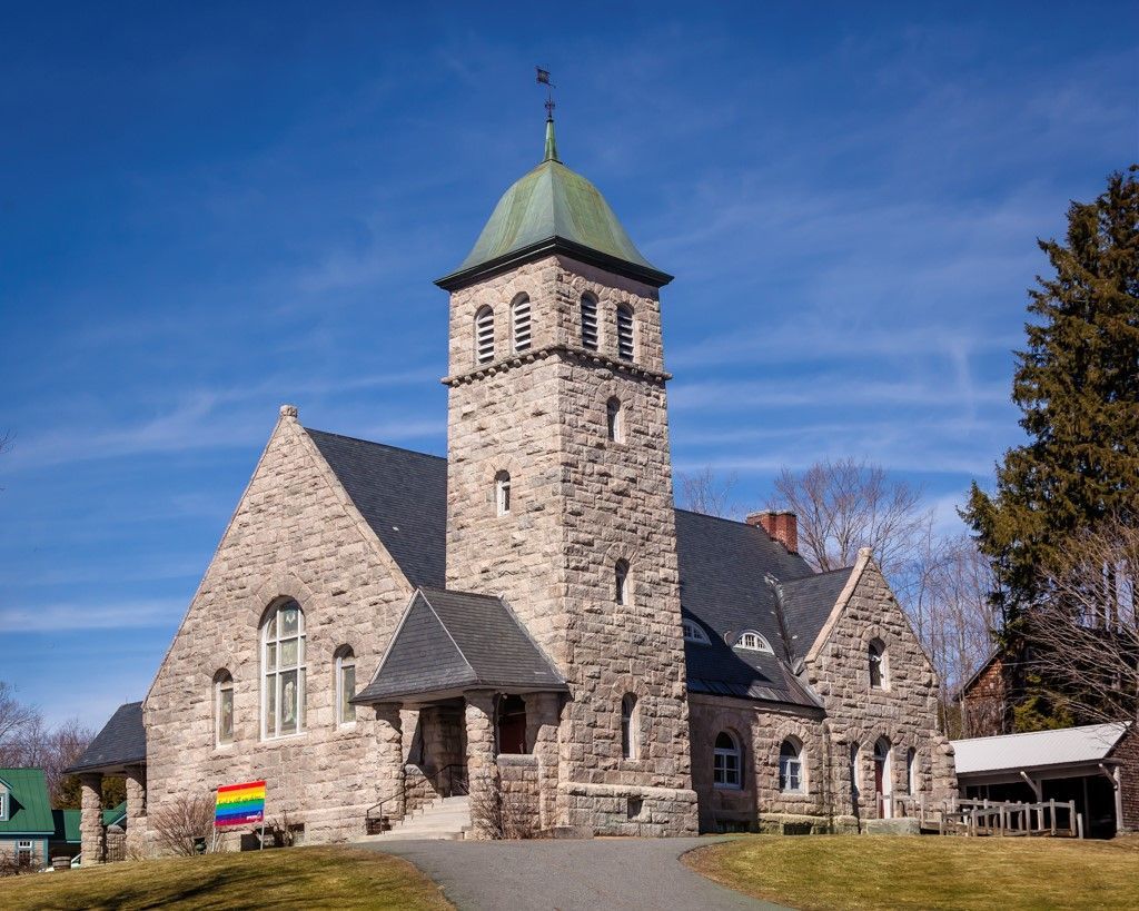A stone church with a green steeple and a rainbow flag in front of it