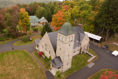 An aerial view of a church in the middle of a forest.