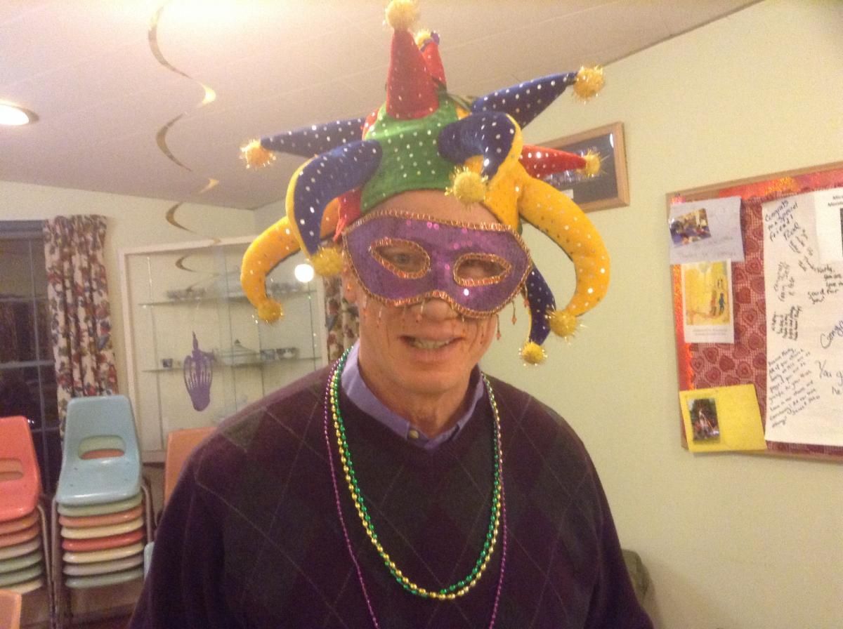 A man wearing a jester hat and a mardi gras mask