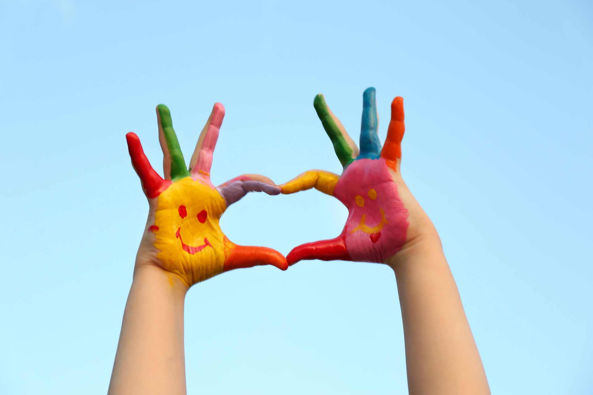 Two painted hands make a heart shape with their fingers