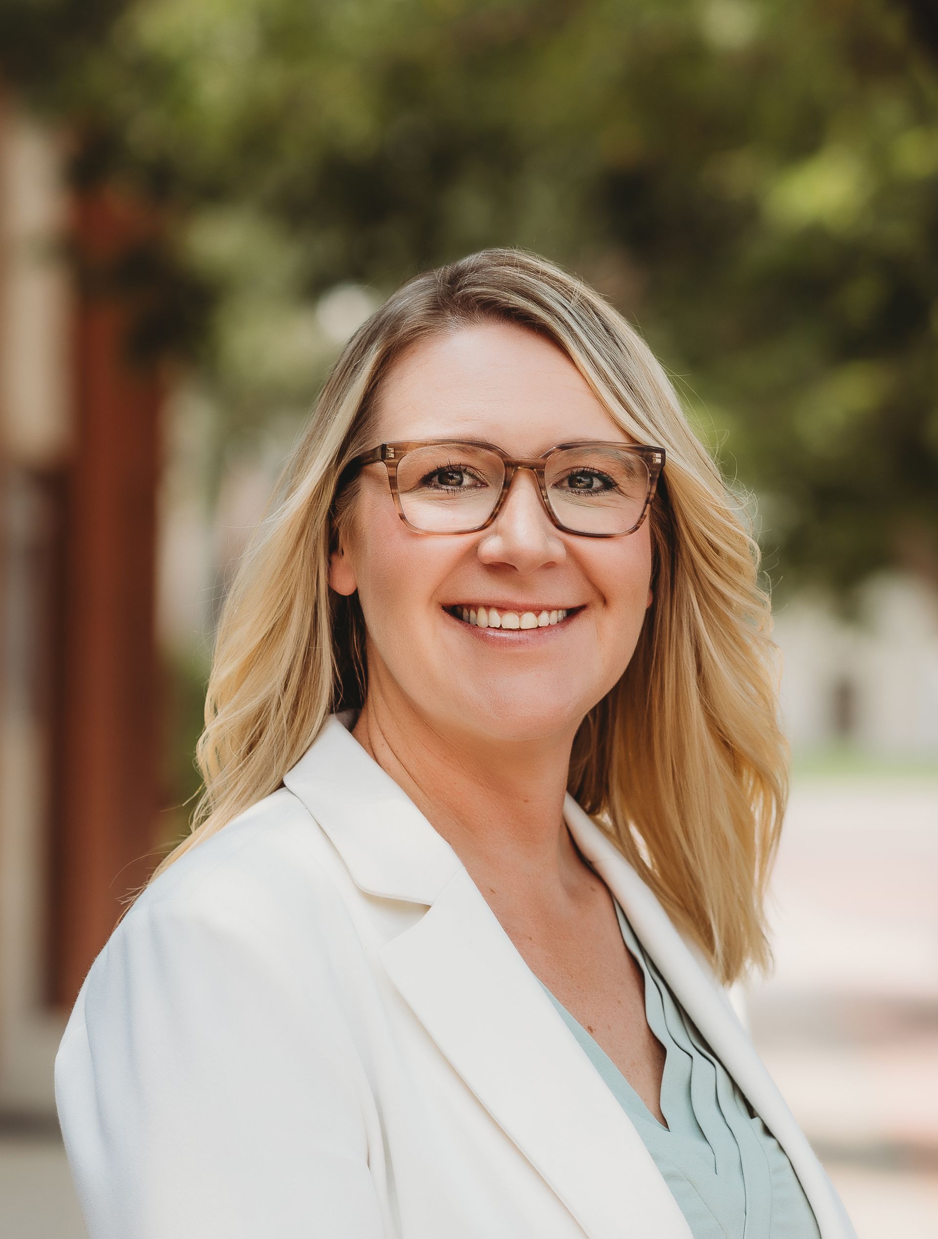 A woman wearing glasses and a white jacket is smiling for the camera.
