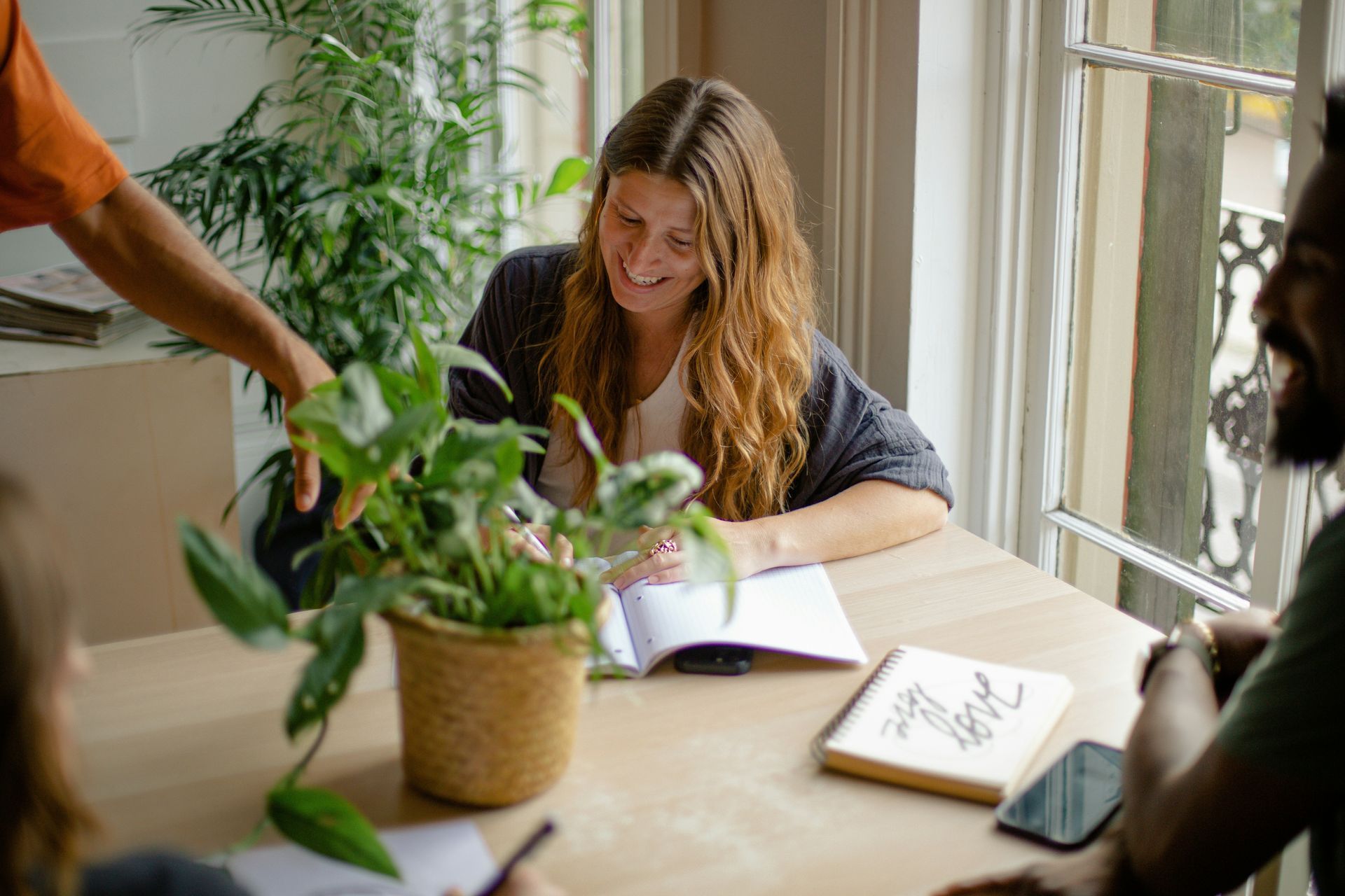 A woman is watering a potted plant while sitting at a table with other people.