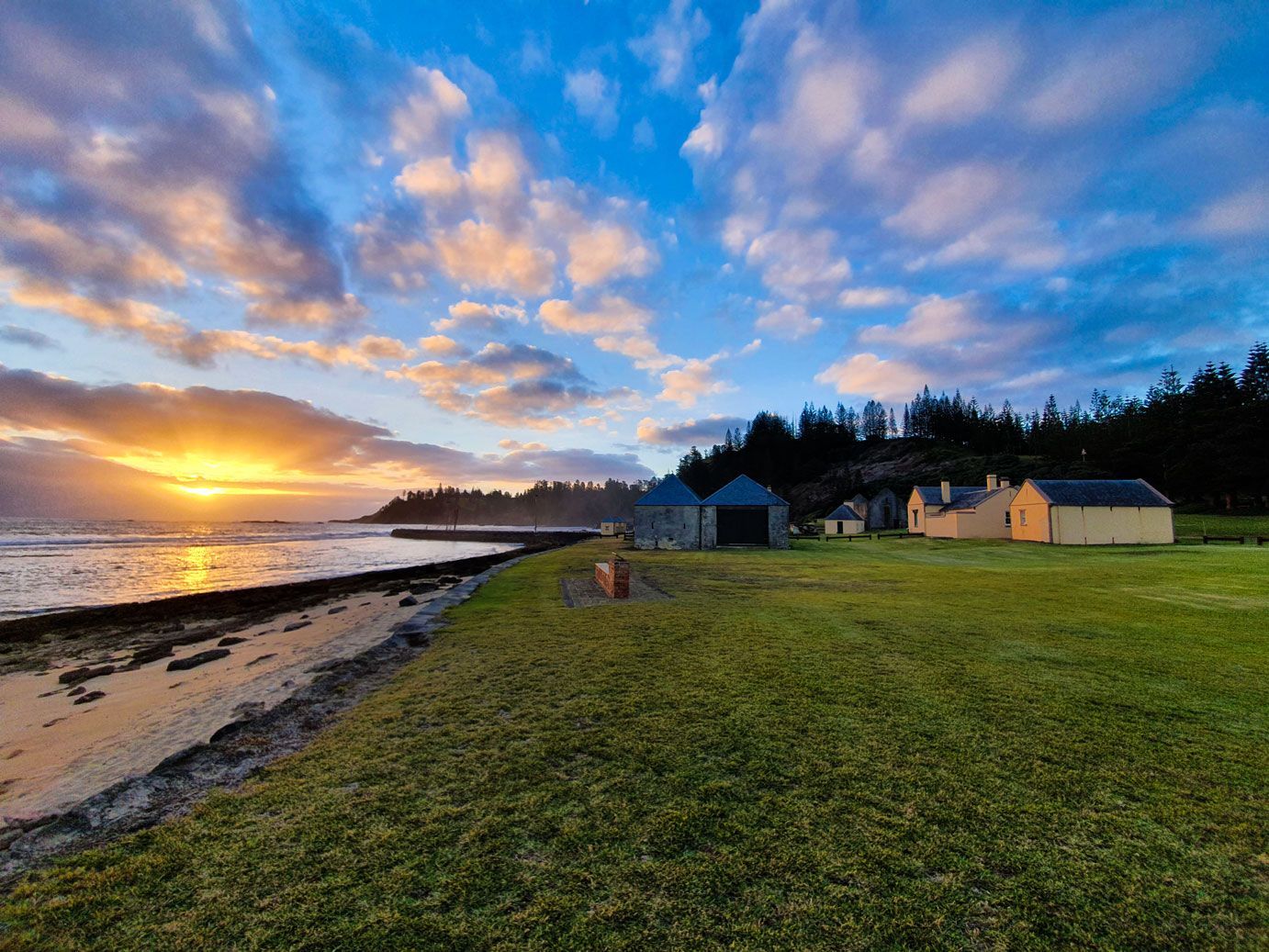 Sunset over the ocean with buildings and a grassy area. Norfolk Island Trade Winds Seniors Sanctuary