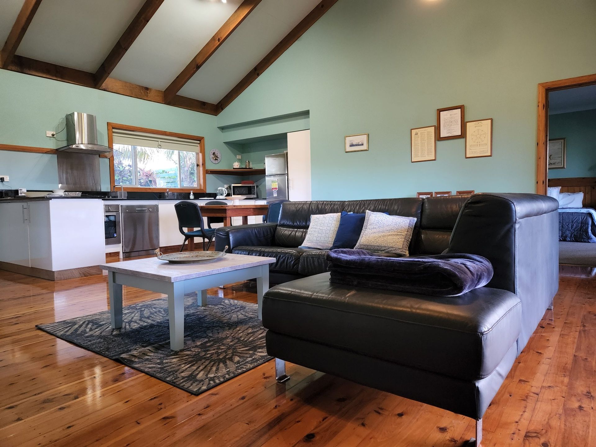 Living room with black leather sectional, hardwood floors. Norfolk Island Trade Winds Seniors Sanctuary