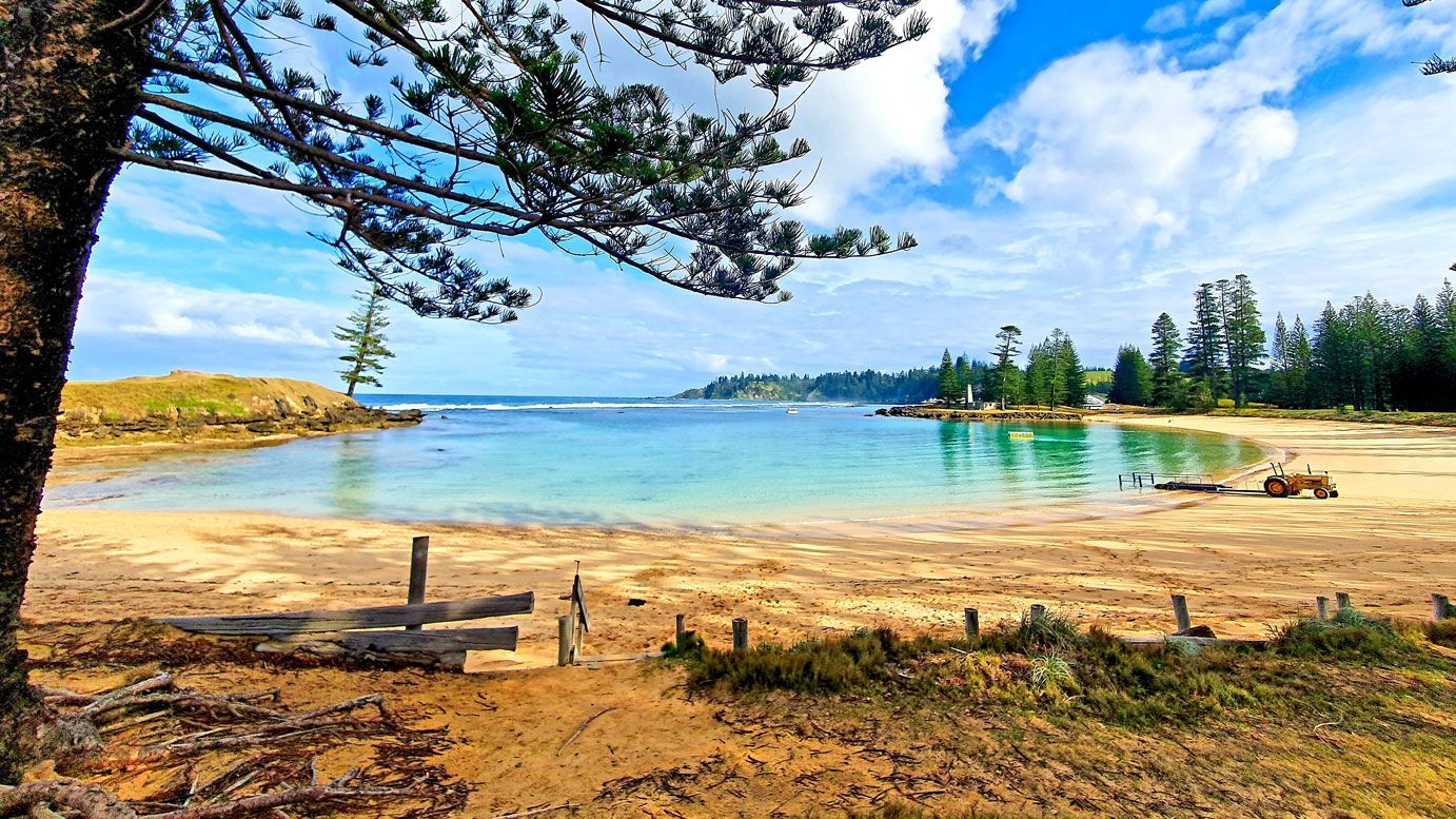 Sandy beach with turquoise water, trees, and blue sky. Norfolk Island Trade Winds Seniors Sanctuary