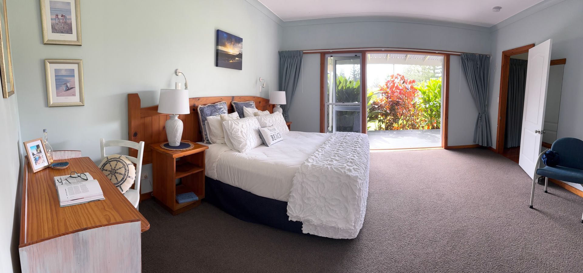 Bedroom with a bed, desk, sliding door to a garden, and a chair. Norfolk Island Trade Winds Seniors Sanctuary