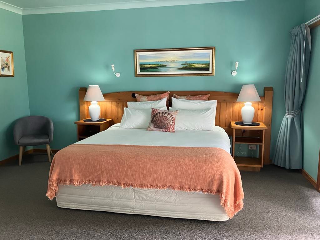 Bedroom with teal walls, a bed with peach blanket, bedside lamps. Norfolk Island Trade Winds Seniors Sanctuary