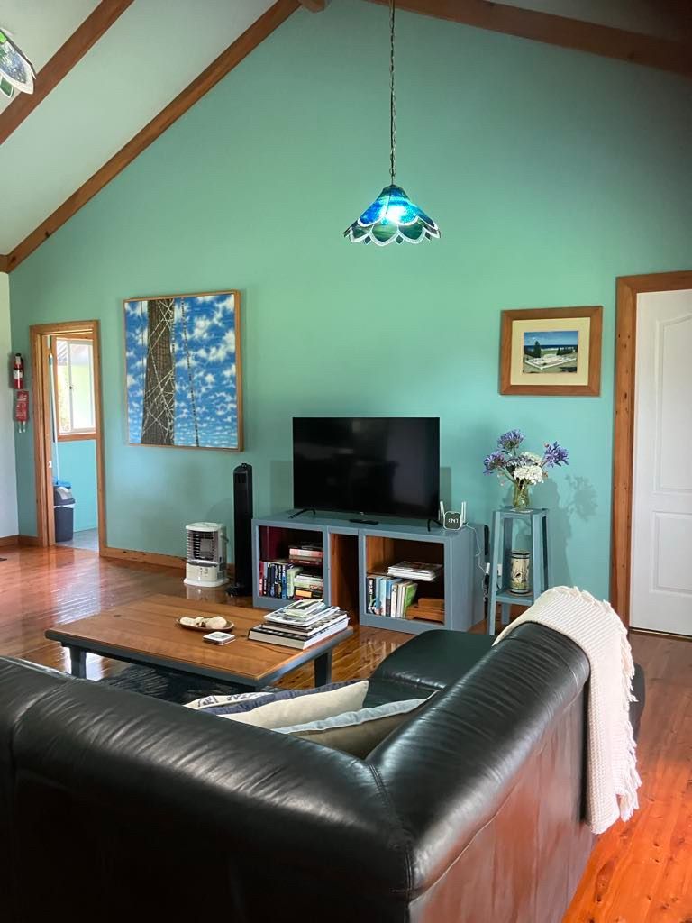 Living room with teal walls, wood floors, black leather couch, and art. Norfolk Island Trade Winds Seniors Sanctuary Flinders