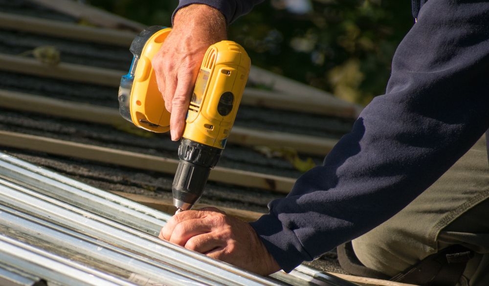 Person Using a Yellow Drill to Secure Metal Roofing to the Frame of a Roof — Roof Tek CQ in Rockhampton, QLD