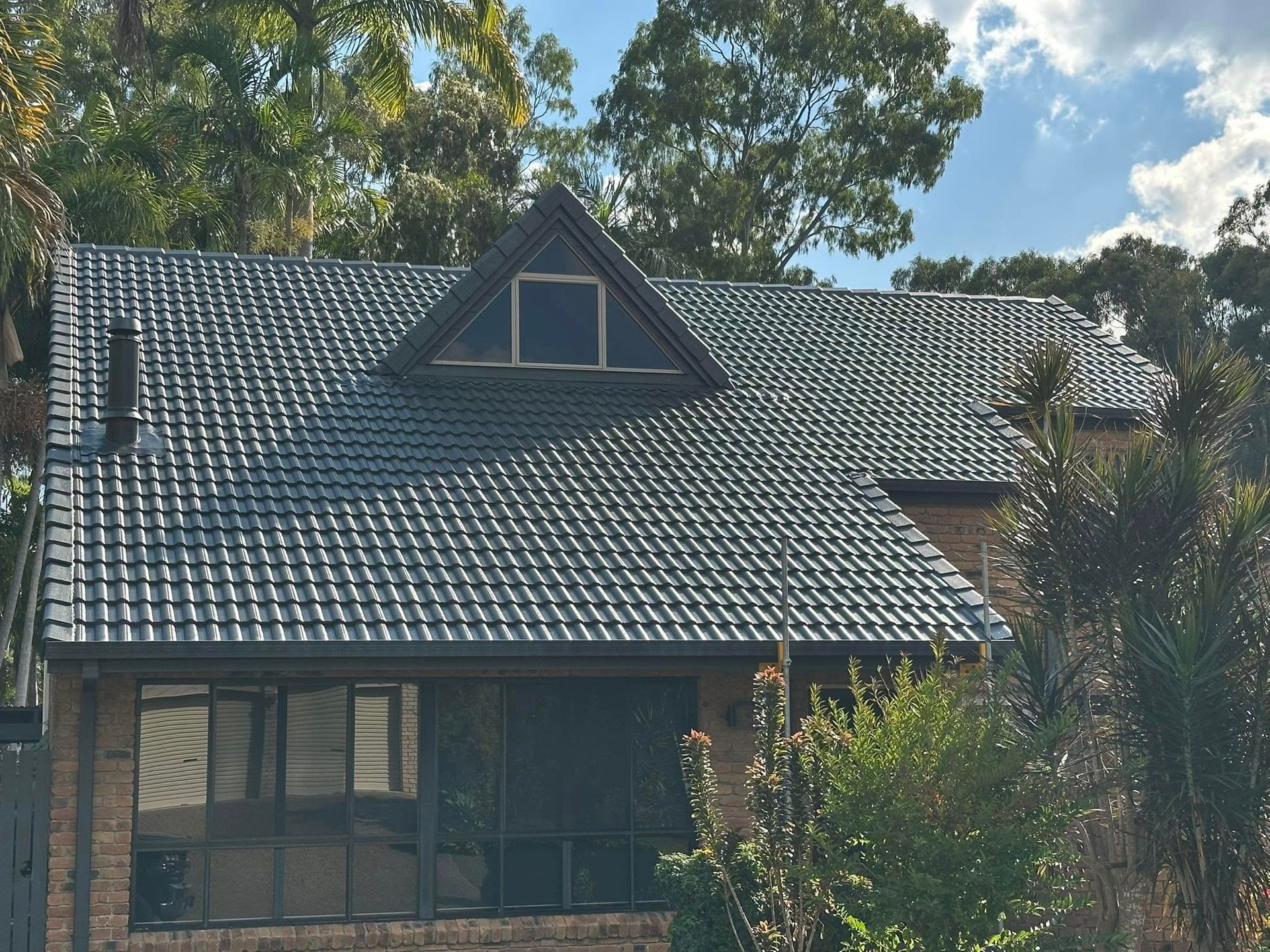 Dark Gray Tiled Roof of a House With a Triangular Window, Surrounded by Trees — Roof Tek CQ in Rockhampton, QLD