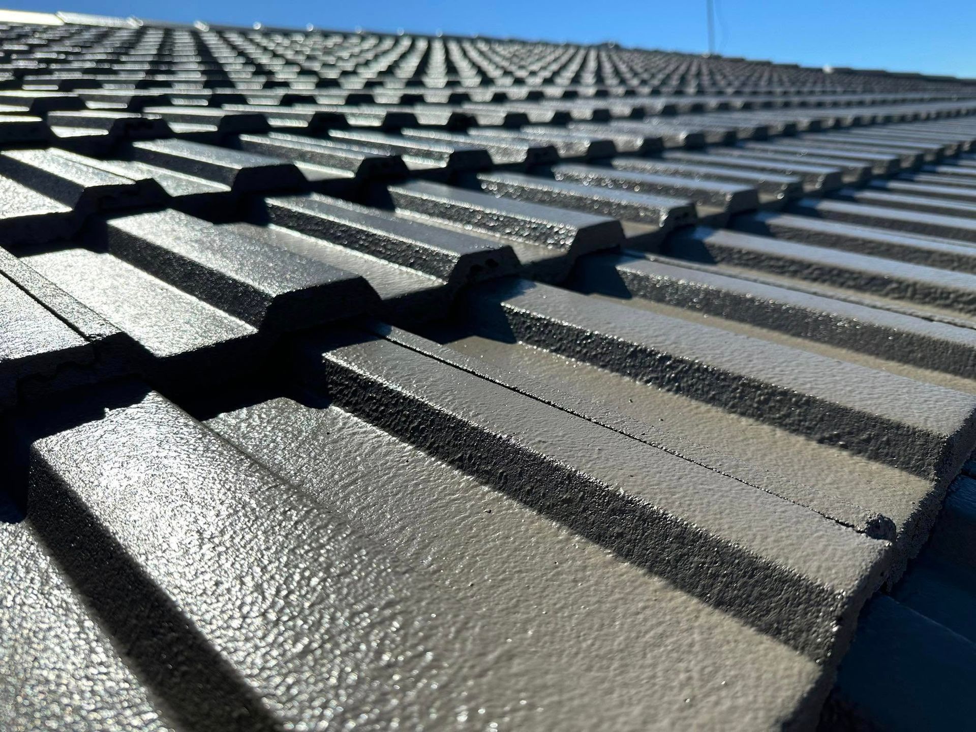 Person in Black Glove Sprays White Paint Onto a Brown Corrugated Roof — Roof Tek CQ in Yeppoon, QLD