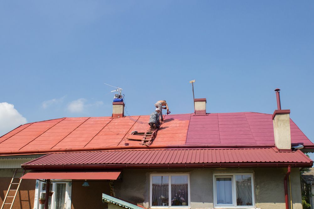 People Painting a Roof Red Against a Blue Sky — Roof Tek CQ in Gracemere, QLD