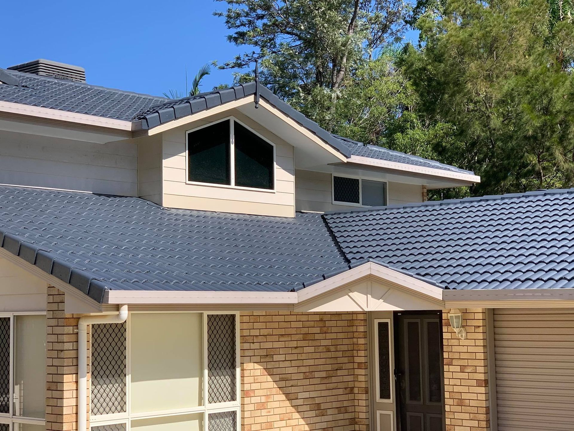 House With Blue Tiled Roof and Beige Brick Exterior; Trees in Background — Roof Tek CQ in Rockhampton, QLD