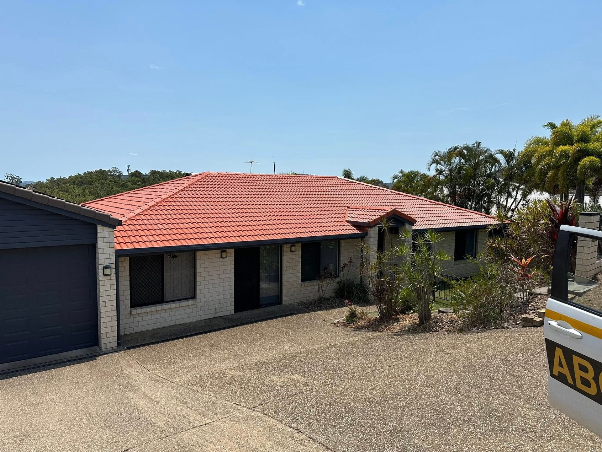 House with orange tile roof, white brick exterior, attached garage, and gravel driveway under a blue sky.