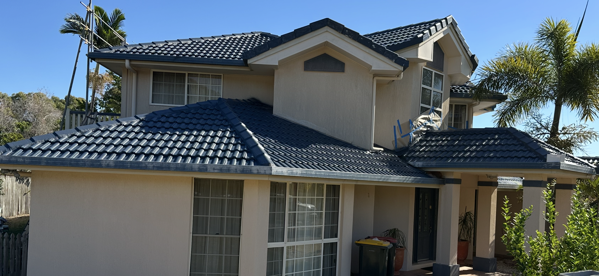 Two-story beige house with a dark blue tiled roof on a sunny day — Roof Tek CQ in Gracemere, QLD