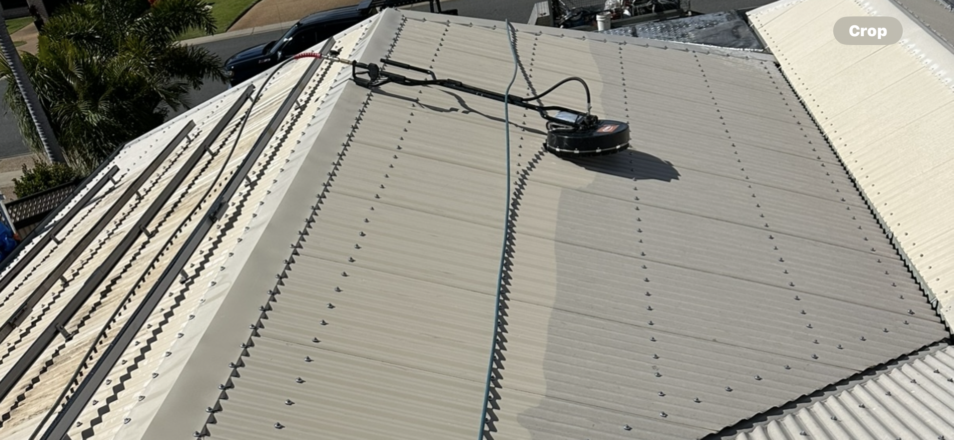 A roof being pressure washed. A cleaning tool is on the gray metal roof — Roof Tek CQ in Gracemere, QLD