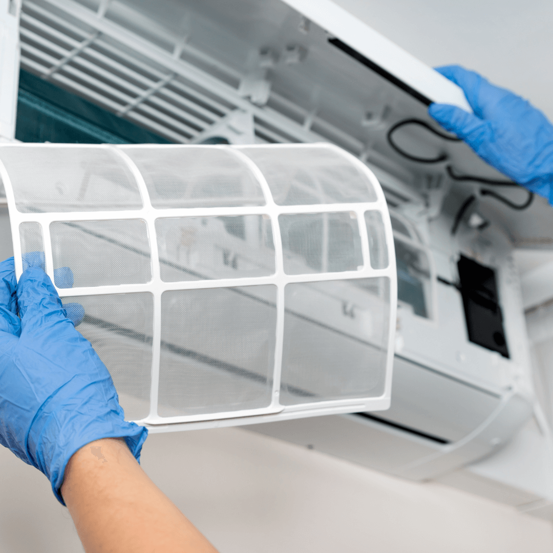 A person wearing blue gloves is cleaning an air conditioner filter.