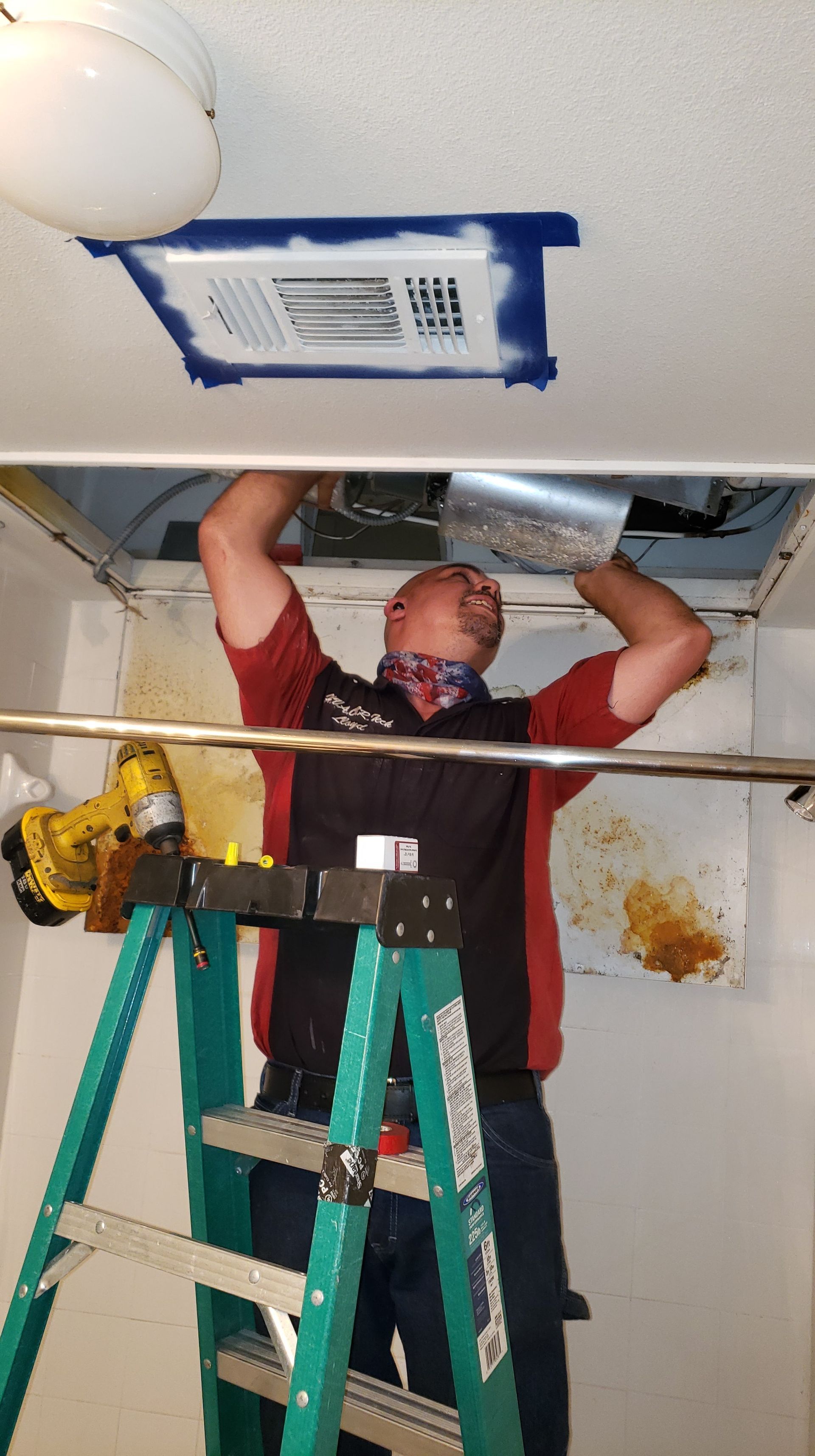 A man is standing on a ladder working on a ceiling fan.