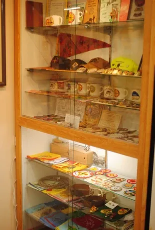 A tall glass display case of a number of scouting graphics and mugs