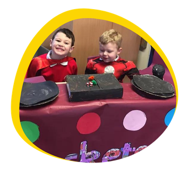 Two young boys are sitting at a table with plates and a book on it