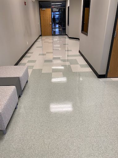 A long hallway with a checkered floor and two ottomans in a building.