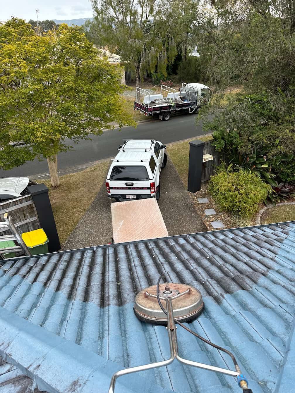 A person is soft washing a blue tiles roof on the Gold Coast.