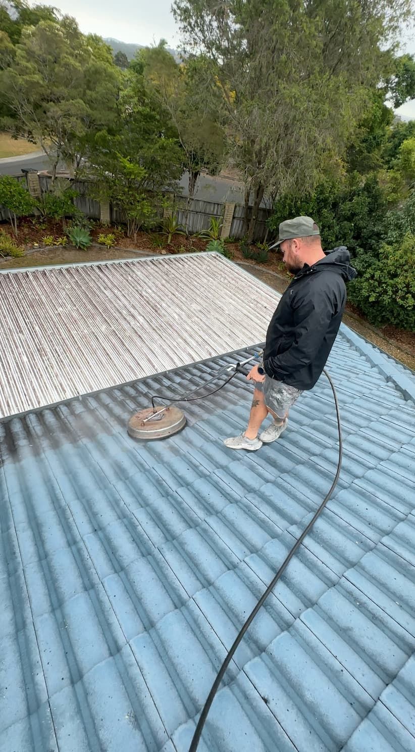 A man is cleaning the roof of a house with a pressure washer.